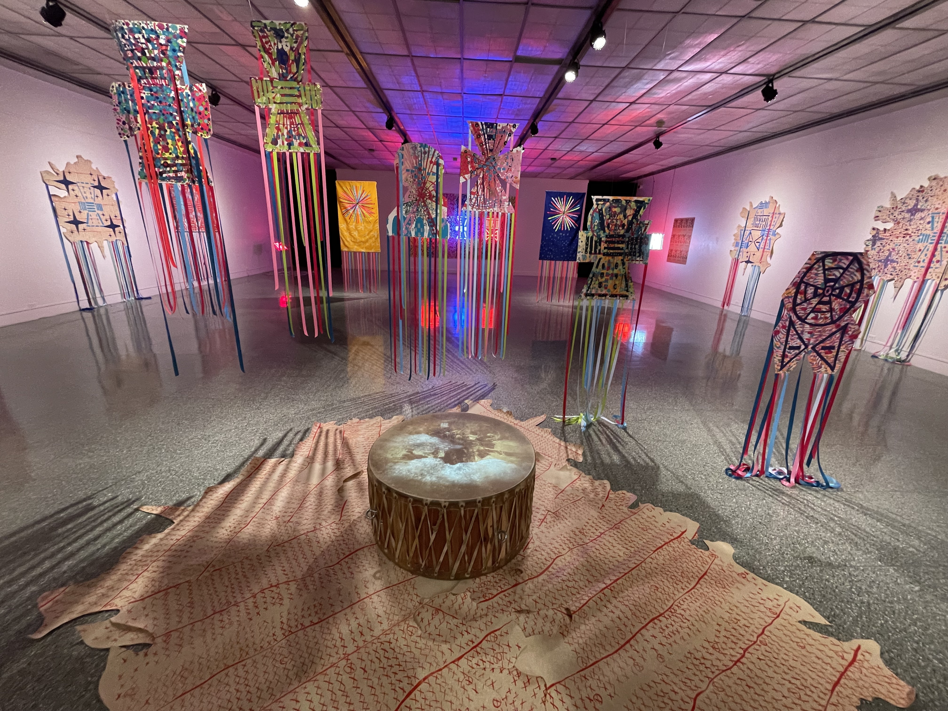 John Hitchcock, Blanket Songs, 2023, Screenprint, lithography, dye on paper, ribbons, grommets, Naugahyde Powwow Drum (Kevin Sovo), video projection, Courtesy of the Artist